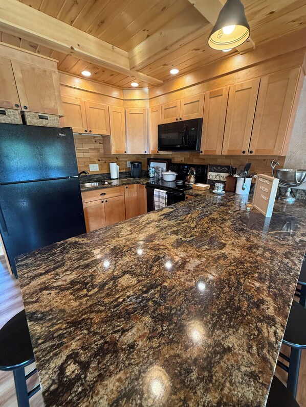 A kitchen with granite countertops, wooden cabinets, a black refrigerator, and a microwave.