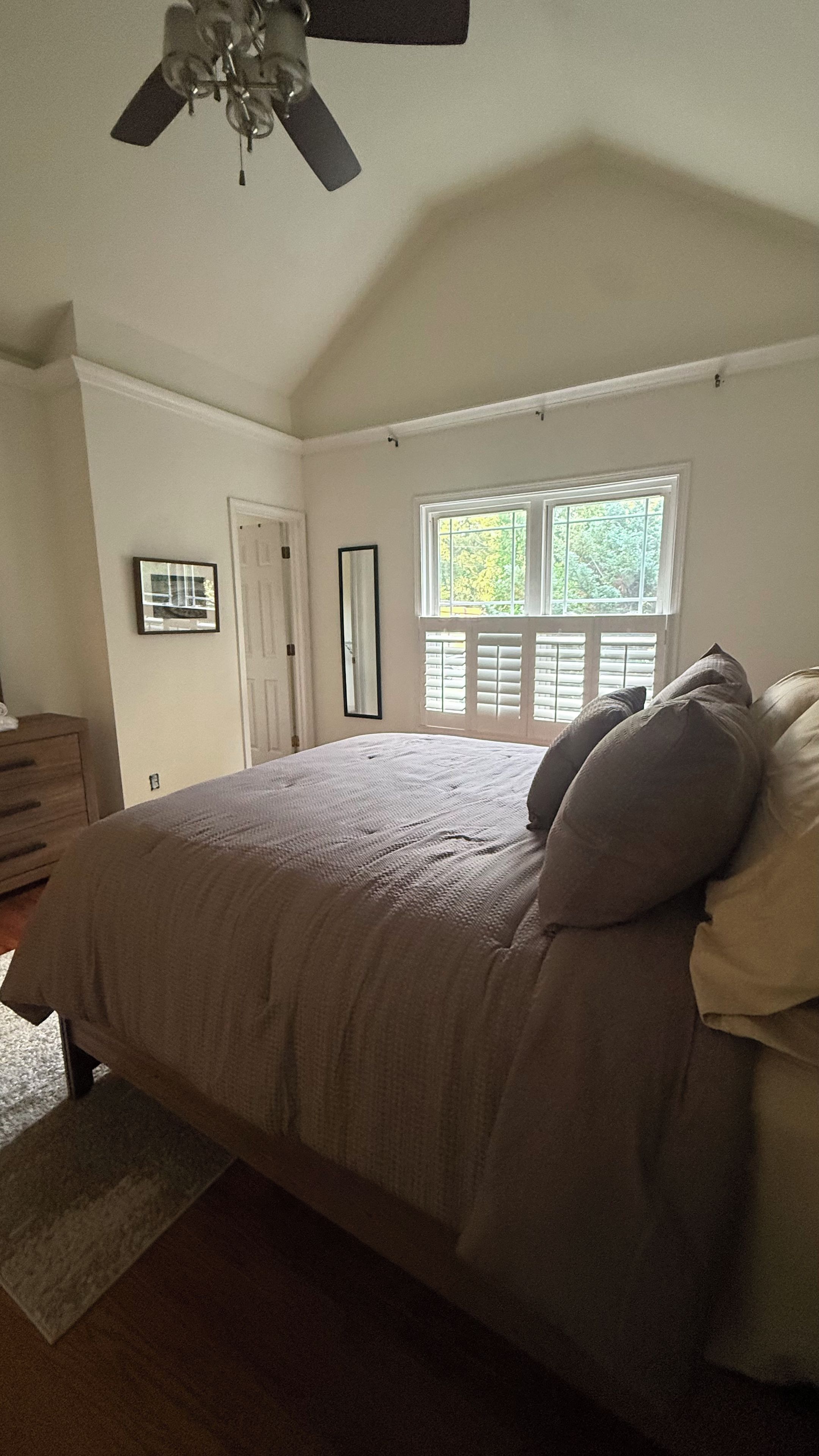 A bedroom with a bed, a ceiling fan, a window with blinds, and a door.