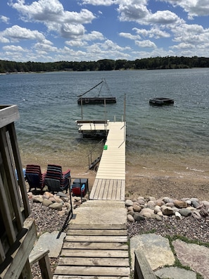 A wooden dock leading to a calm lake with boats, surrounded by a wooden structure with chairs and a table. - Sandy beach, hot tub, amazing sunsets, spacious lake home, kayaks and more. (Wautoma)