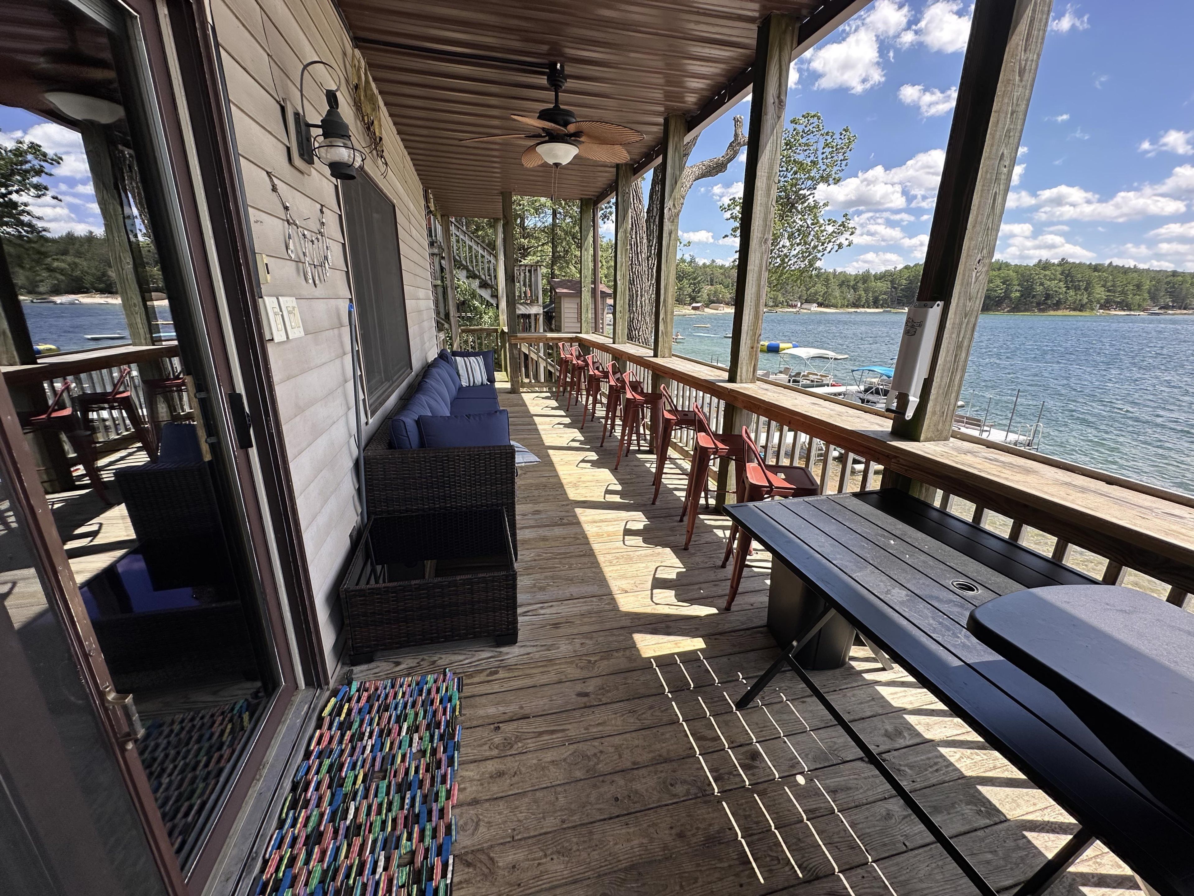 A covered deck with outdoor seating, a view of the lake, and a wooden railing.