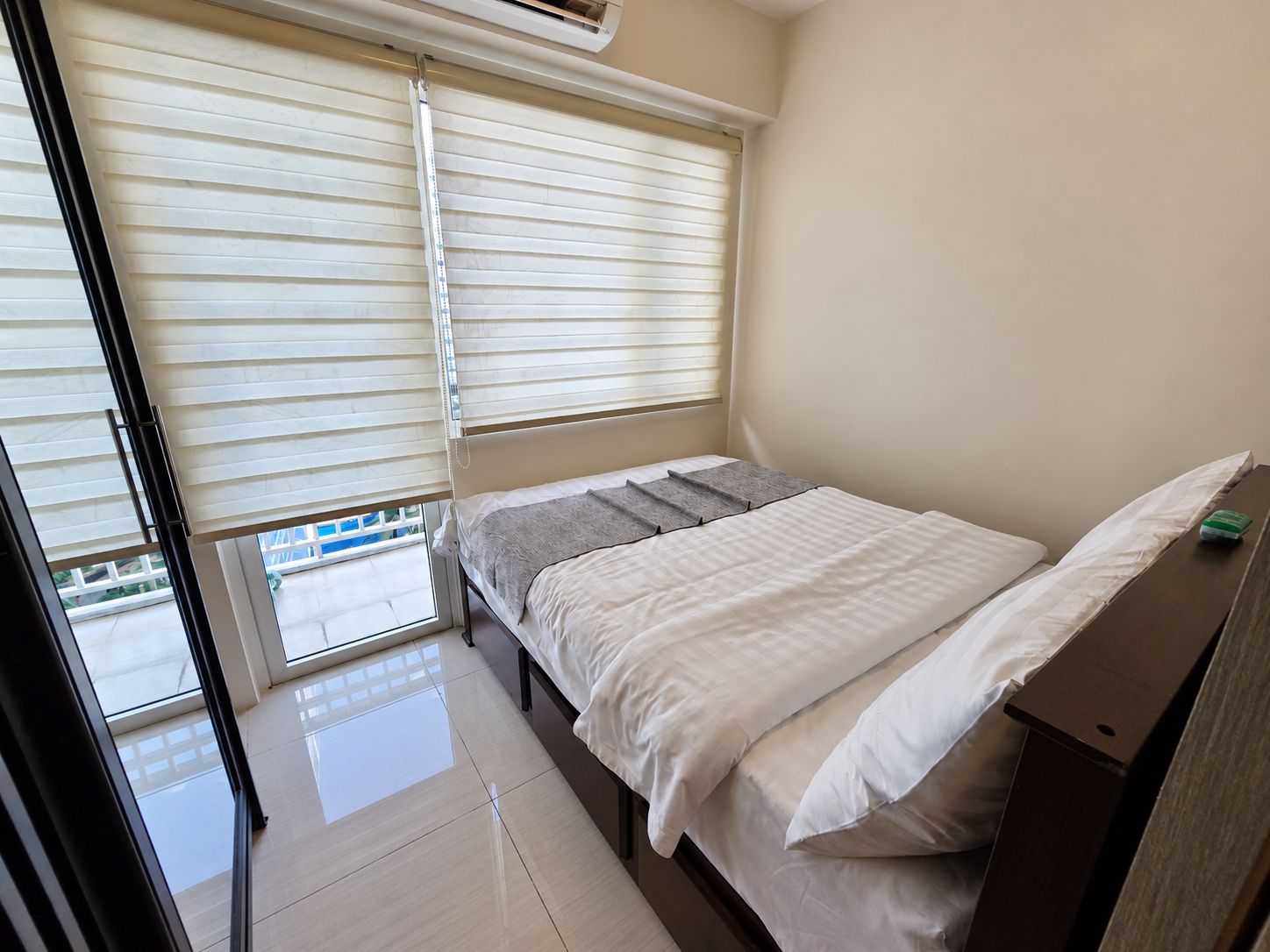 Une chambre à coucher avec un lit, une table de chevet, une fenêtre avec des stores et une vue sur l’extérieur.