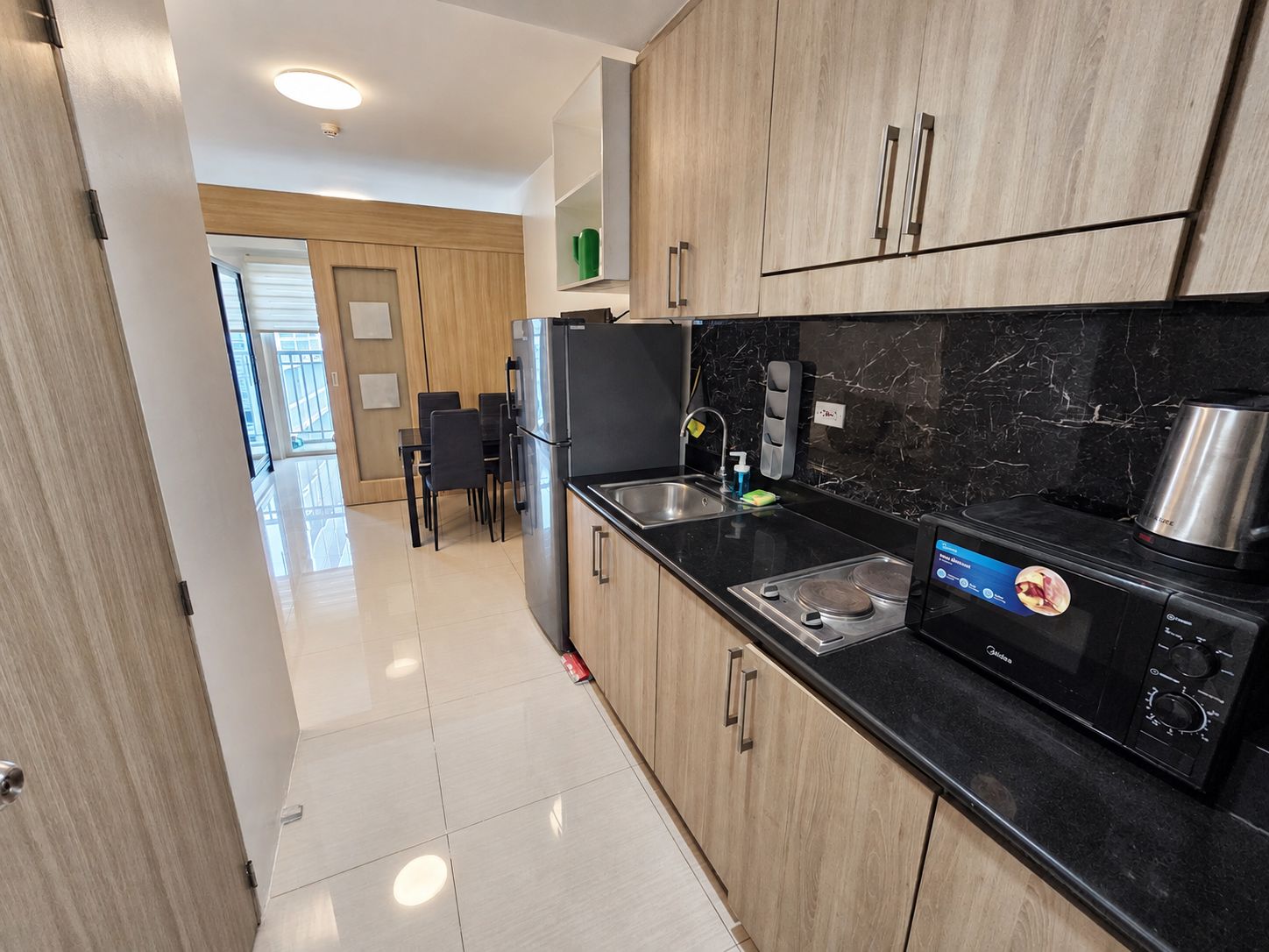 Una cocina moderna con armarios de madera, encimera negra y electrodomésticos de acero inoxidable.