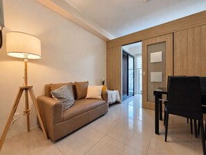 A modern living room with a sofa, a lamp, a dining table, and a sliding door leading to another room. - Shore 1 Residences by LUXE (Pasay City)