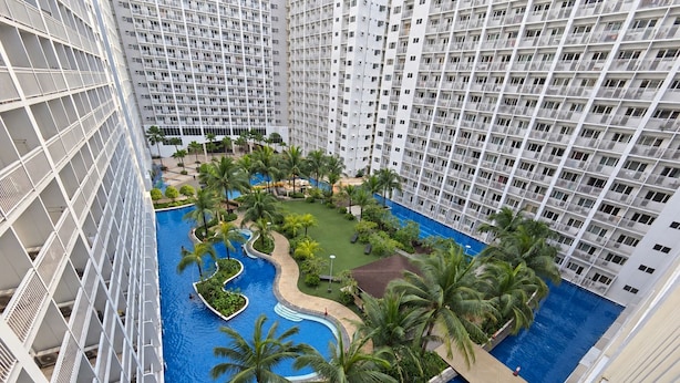 A high-rise hotel with a central swimming pool surrounded by palm trees and greenery. - Shore 1 Residences by LUXE (Pasay City)