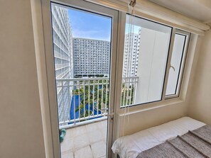 Un dormitorio con balcón, cama y vistas a un edificio y una piscina.