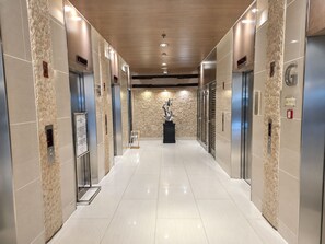 A modern elevator lobby with a polished floor, wall-mounted elevators, and a central sculpture. - Shore 1 Residences by LUXE (Pasay City)
