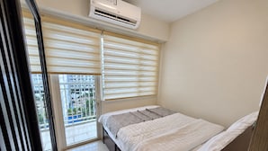 A bedroom with a bed, a window with blinds, an air conditioning unit, and a view of a building outside. - Shore 1 Residences by LUXE (Pasay City)