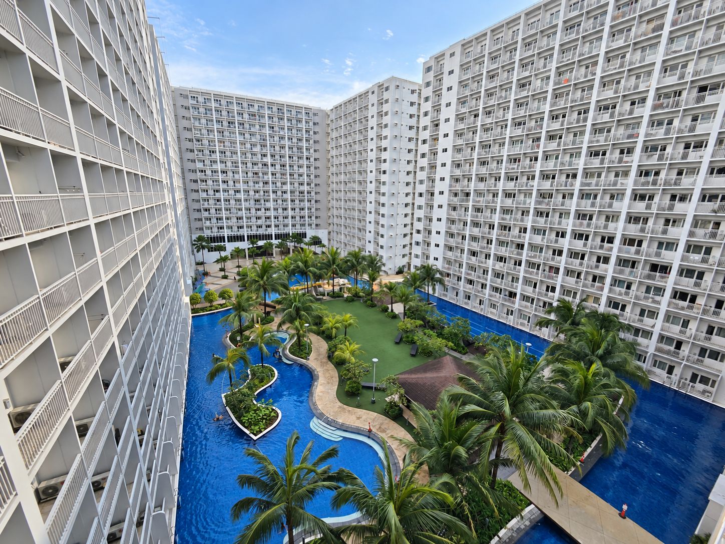 Un hôtel de grande hauteur doté de nombreux balcons, d’une piscine centrale et entouré de verdure.