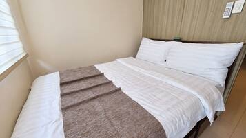 Una cama individual con ropa de cama blanca y una manta marrón, un cabecero de madera y un panel de control en la pared.