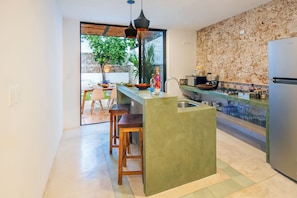 Eine moderne Küche mit Kochinsel, Barhocker, Spüle und Blick ins Freie.