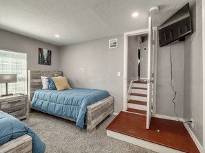 A bedroom with a bed, a TV, a painting, and a staircase. - Cozy 4-bed retreat. Blocks from OU. Family-friendly with yard games and firepit! (Norman)