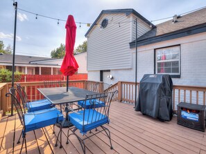 A deck with a table and chairs, a red umbrella, and a barbecue grill. - Cozy 4-bed retreat. Blocks from OU. Family-friendly with yard games and firepit! (Norman)