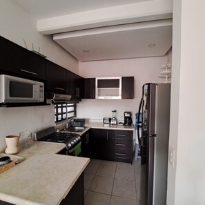 A kitchen with dark cabinets, a microwave, stove, and a refrigerator. - Residencial Alborada: Relaxation with a Caribbean Spirit (Puerto Morelos)