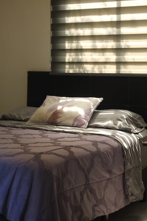 A bed with a patterned bedspread and a pillow, a headboard, and a window with blinds. - Residencial Alborada: Relaxation with a Caribbean Spirit (Puerto Morelos)