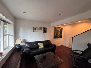 A modern living room with a black leather sofa, a glass coffee table, and a black armchair. There are framed pictures on the wall and a large abstract painting. - Scandinavian Japanese Inspired Modern Sunny Private Home Nestled in Nature (Santa Cruz)