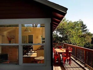 A wooden deck with a dining table and chairs, a glass door leading to an interior space with a dining area, and a view of trees. - Scandinavian Japanese Inspired Modern Sunny Private Home Nestled in Nature (Santa Cruz)