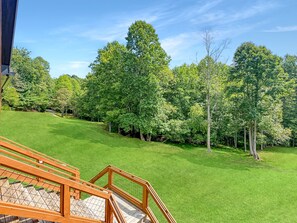 A wooden deck with a view of a well-maintained lawn and trees. - Blue Ridge Serenity - Creekside | Hot Tub | Firepit | Wildlife Galore! (Morganton)