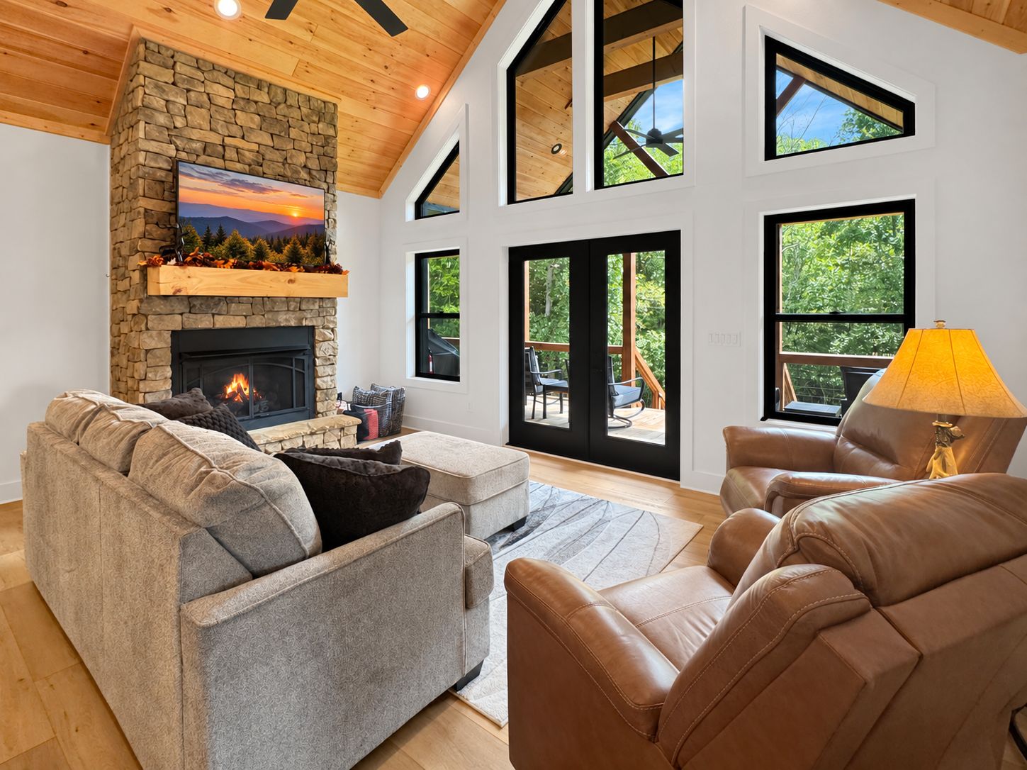 A modern living room with a stone fireplace, leather sofas, and large windows offering views of the outdoors.