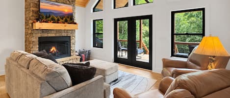 A modern living room with a stone fireplace, leather sofas, and large windows offering views of the outdoors.