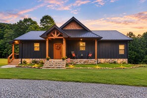 A two-story house with a stone foundation, a wooden front porch, and a metal roof. - Blue Ridge Serenity - Creekside | Hot Tub | Firepit | Wildlife Galore! (Morganton)