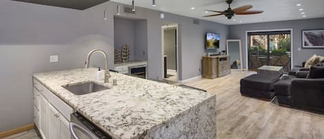 A modern kitchen with a granite countertop, built-in dishwasher, and a ceiling fan.