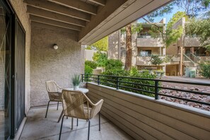 A balcony with two wicker chairs and a table, overlooking a landscaped area with trees and a building in the background. - Old Town Scottsdale Oasis&Heated Pools&Golf&Gym (Scottsdale)