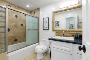 A modern bathroom with a glass-enclosed shower, a white toilet, a sink with a dark countertop, and a large mirror above the sink.