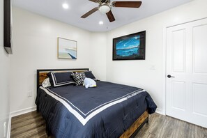 Ein Schlafzimmer mit Bett, Deckenventilator, Kunstwerken und einer weißen Tür.
