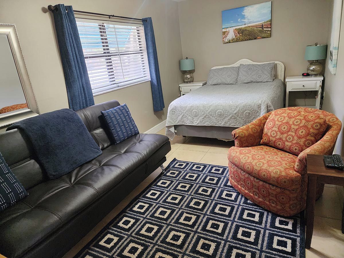 Une chambre à coucher avec un lit, un canapé, une chaise, une fenêtre avec des rideaux et un tableau au mur.