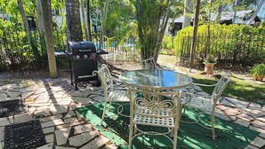 An outdoor patio with a round glass table and white metal chairs, surrounded by a stone-tiled floor and green artificial turf. - Naples Inn & Docks (Naples)