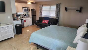 A compact room with a bed, a sofa, a small kitchenette, and a TV.