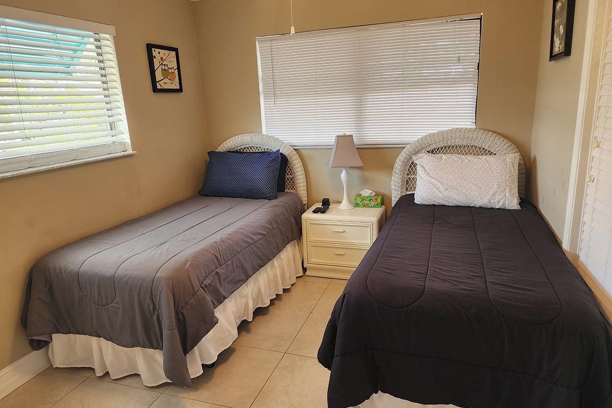 A bedroom with two single beds, a nightstand with a lamp, and a window with blinds.