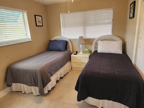 A bedroom with two single beds, a nightstand with a lamp, and a window with blinds. - Naples Inn & Docks (Naples)