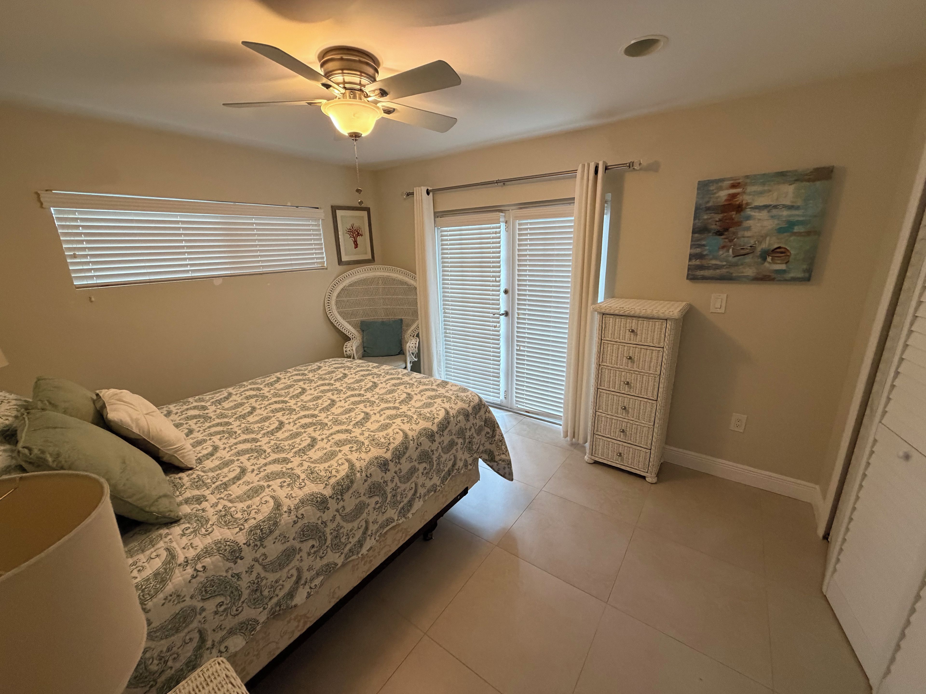 A bedroom with a bed, a chair, a dresser, a ceiling fan, and a window with blinds.