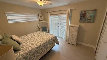 A bedroom with a bed, a chair, a dresser, a ceiling fan, and a window with blinds.