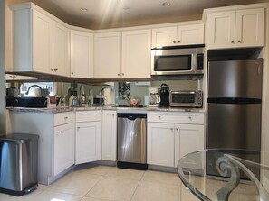 A modern kitchen with white cabinets, stainless steel appliances, and a glass dining table.