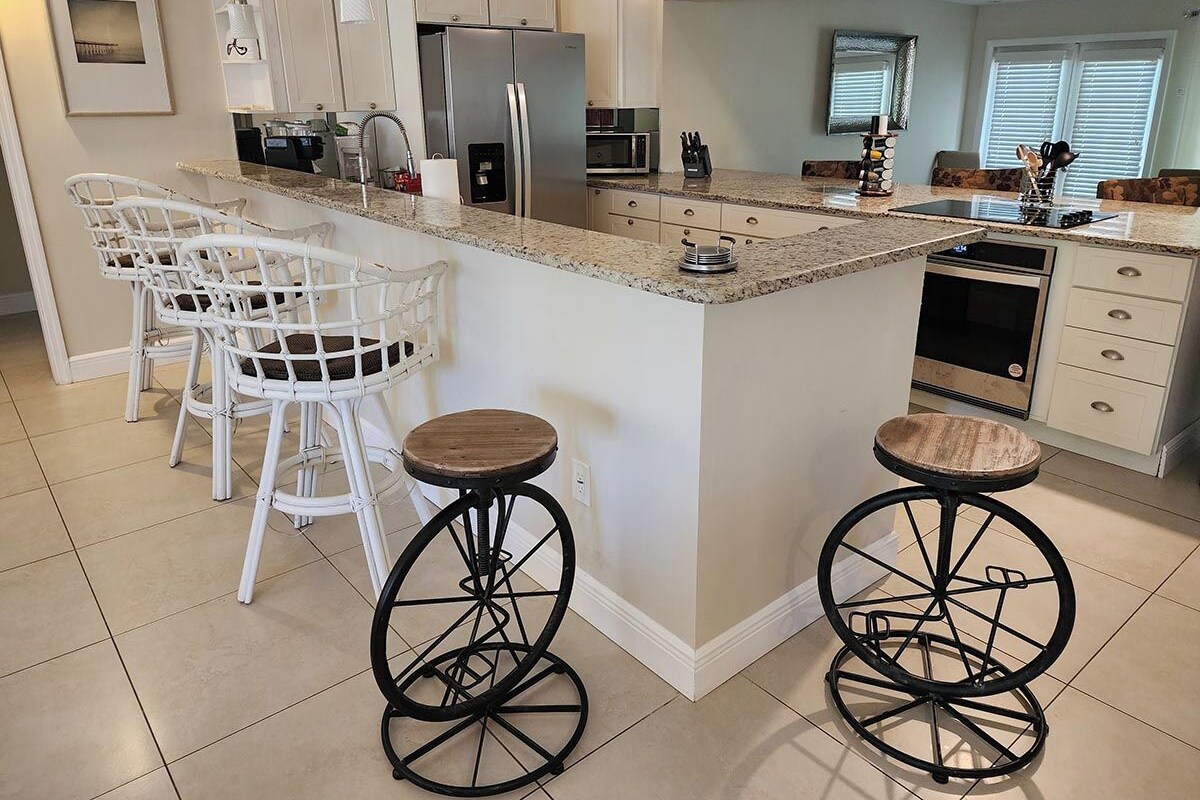 A kitchen with white bar stools, a refrigerator, microwave, and a dishwasher.