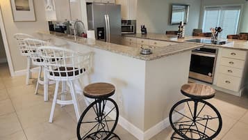 Una cocina con taburetes blancos, refrigerador, microondas y lavavajillas.