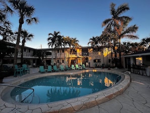 A pool area with lounge chairs and palm trees, surrounded by a building with balconies. - Naples Inn & Docks (Naples)