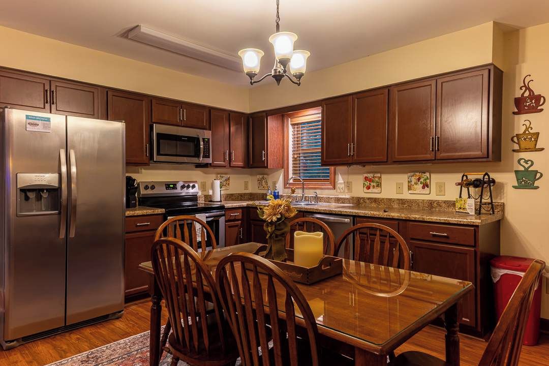A kitchen with wooden cabinets, stainless steel appliances, a dining table with chairs, and a chandelier.