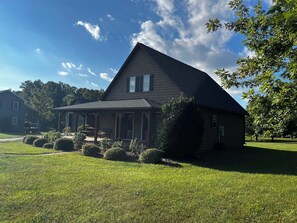 Uma casa de dois andares com varanda coberta, gramado e uma grande árvore.