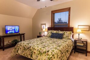 Quarto com uma cama, televisão sobre um móvel, janela com persianas e duas luminárias de cabeceira.