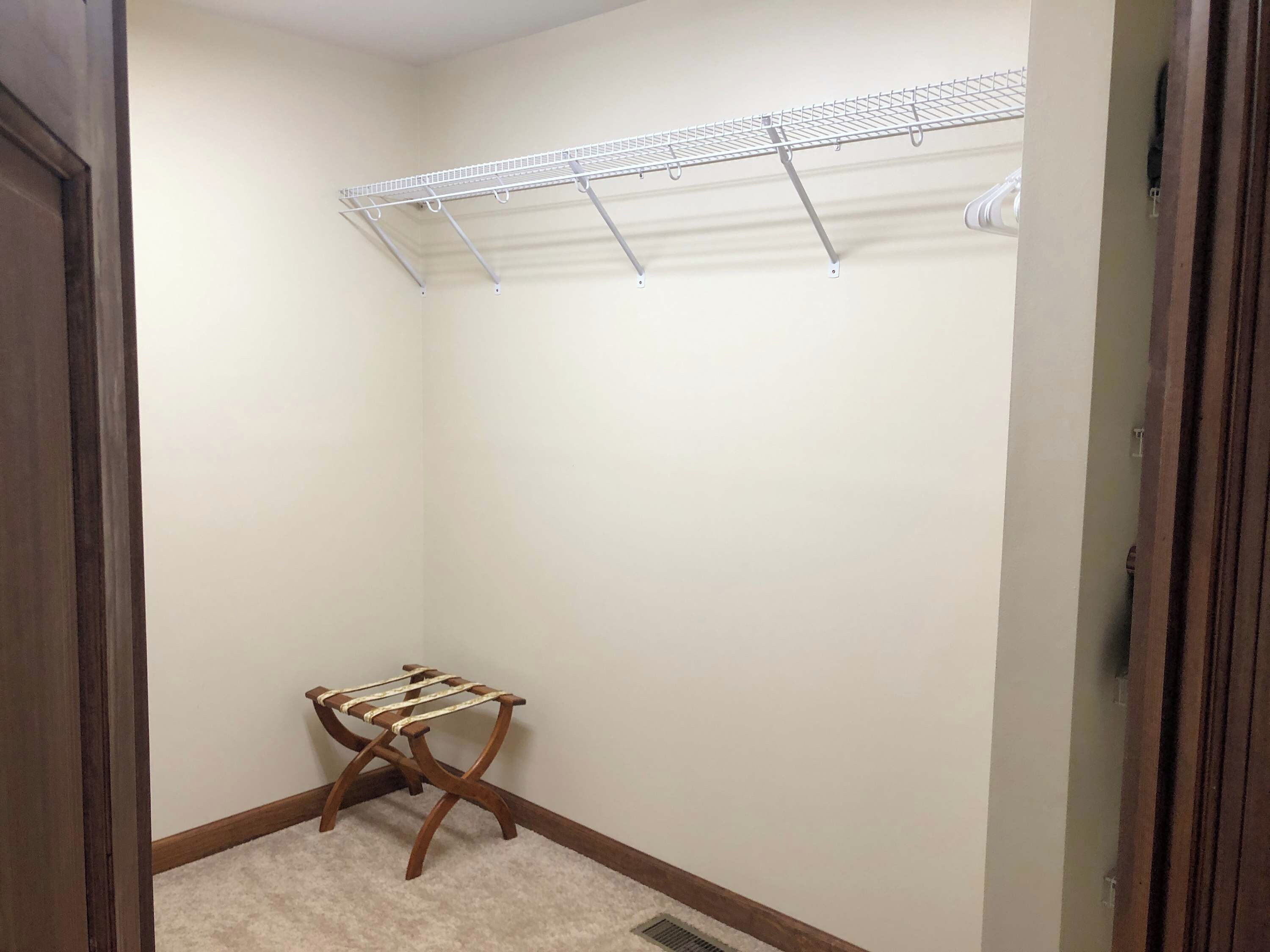 A walk-in closet with a metal drying rack, a wooden drying rack, and a carpeted floor.