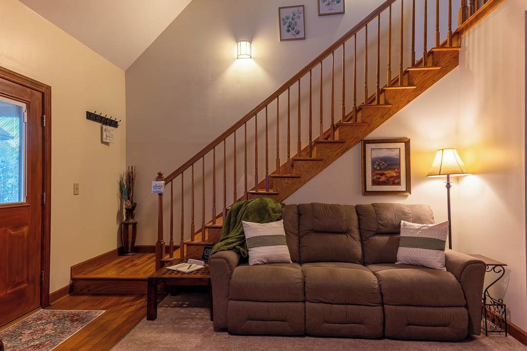 Una sala de estar con un sofá marrón, una escalera de madera y una lámpara.