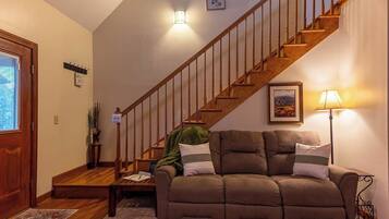 Una sala de estar con un sofá marrón, una escalera de madera y una lámpara.