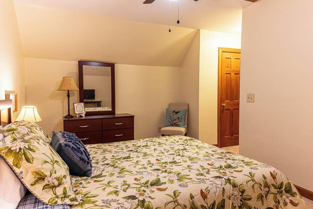 Un dormitorio con cama, cómoda, silla, lámpara, espejo y puerta.