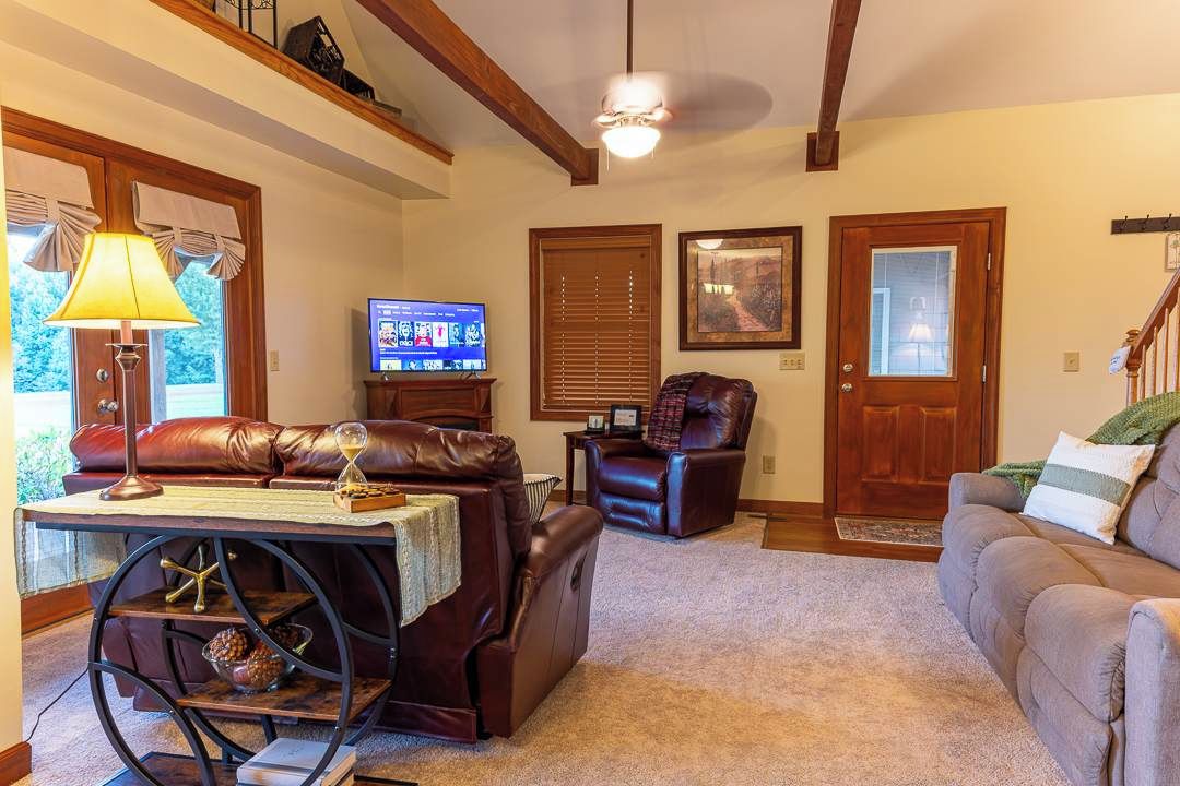 A living room with a leather sofa, a recliner, a coffee table with a lamp, a television, and a staircase.