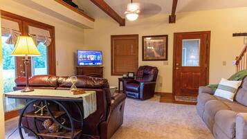 A living room with a leather sofa, a recliner, a coffee table with a lamp, a television, and a staircase.