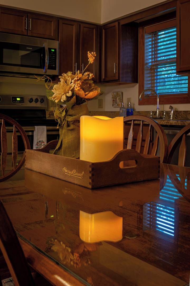 A wooden dining table with a reflective surface, a candle in a wooden tray, and a bouquet of dried flowers.