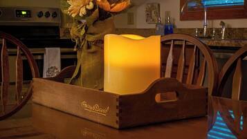A wooden dining table with a reflective surface, a candle in a wooden tray, and a bouquet of dried flowers.